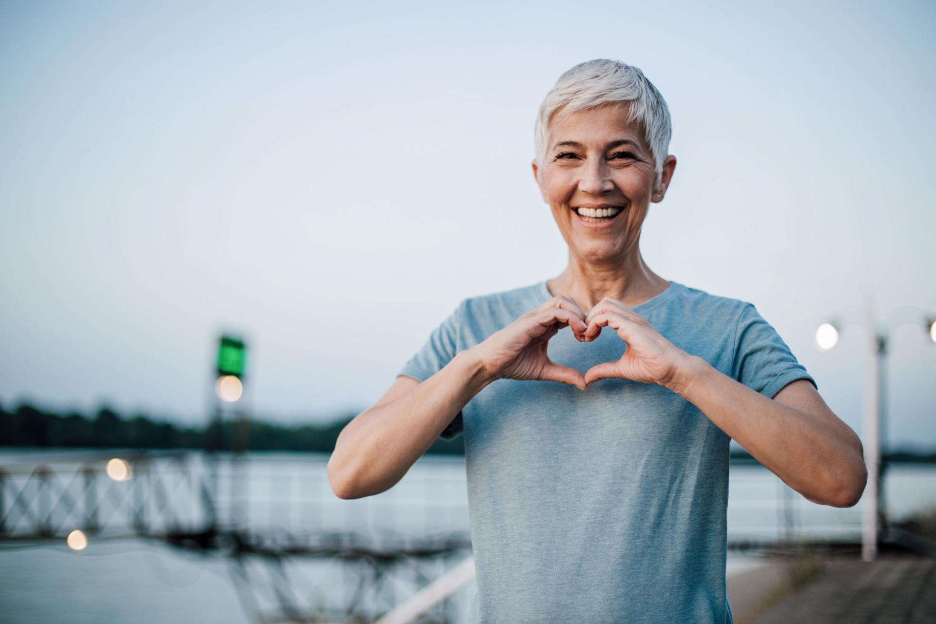 Ältere Krebskranke Frau ist glücklich und zeigt ein Herz mit ihren Händen.