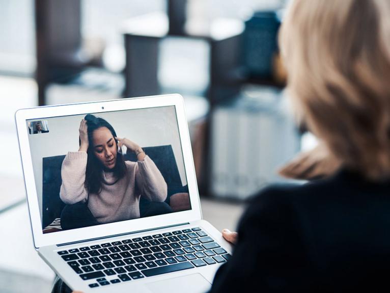 Frau mit blonden Haaren sitzt vor dem Laptop und spricht mit einer anderen Frau über einen Videoanruf