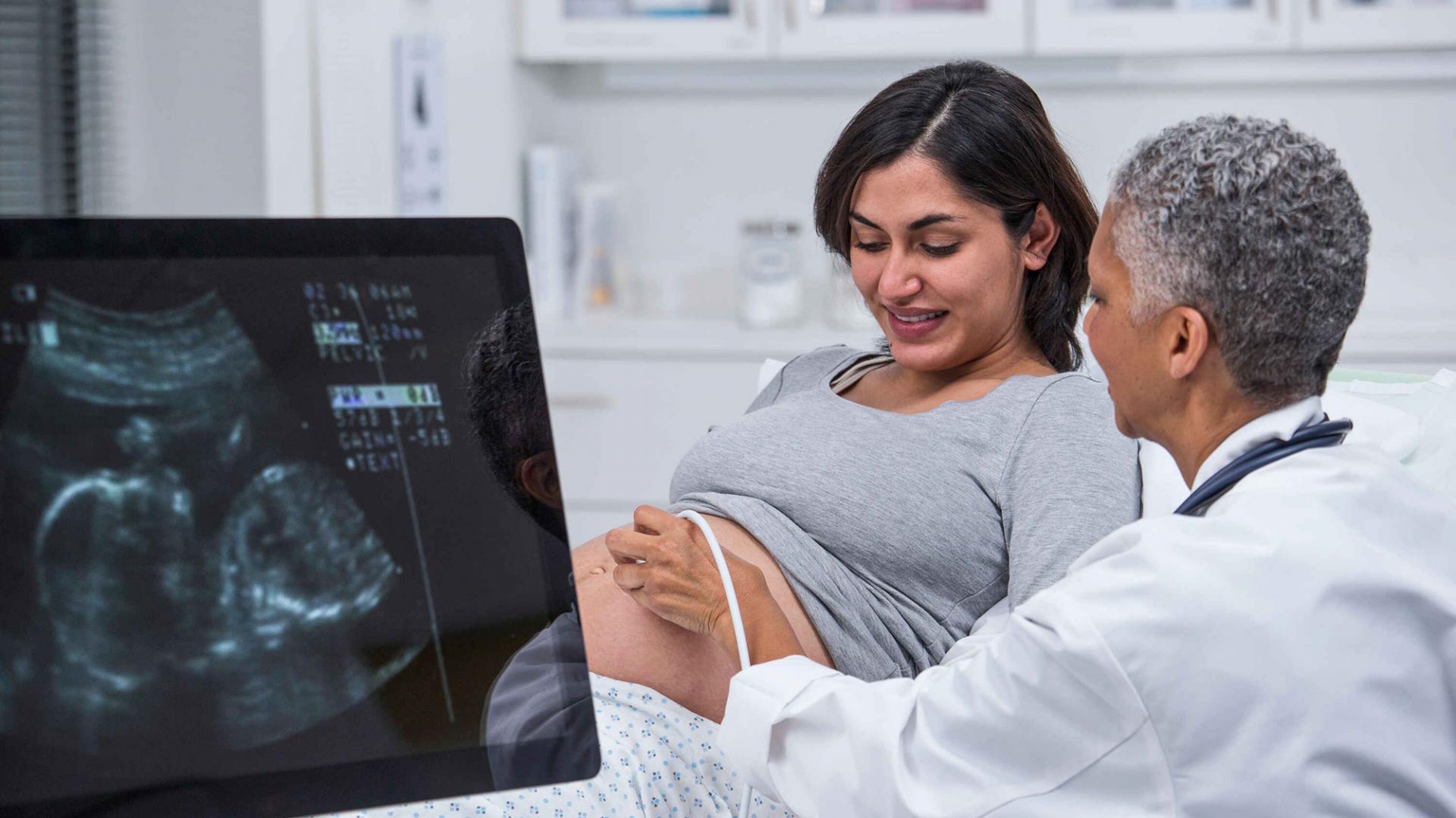 Eine schwangere Frau liegt auf der Untersuchungsliege bei der Gynäkologin und lässt einen Ultraschall machen.