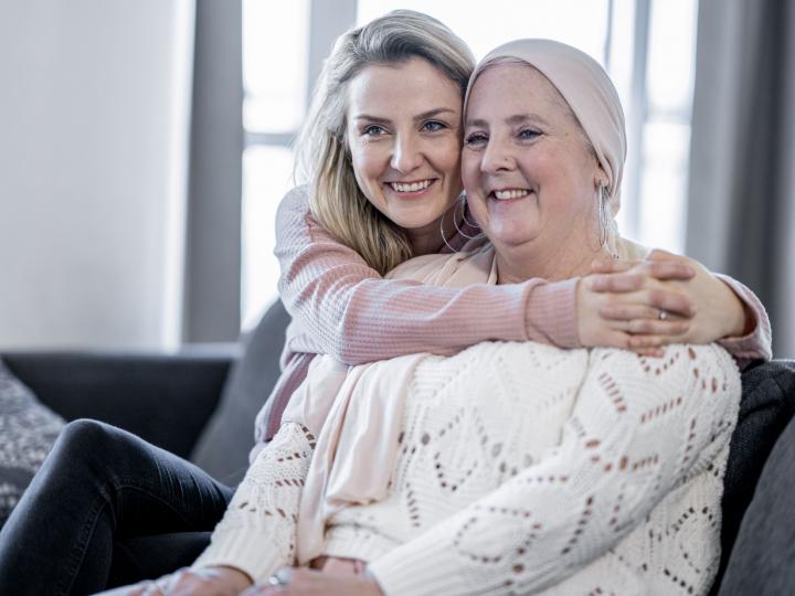 Krebskranke Mutter und Tochter sitzen auf der Couch und umarmen sich