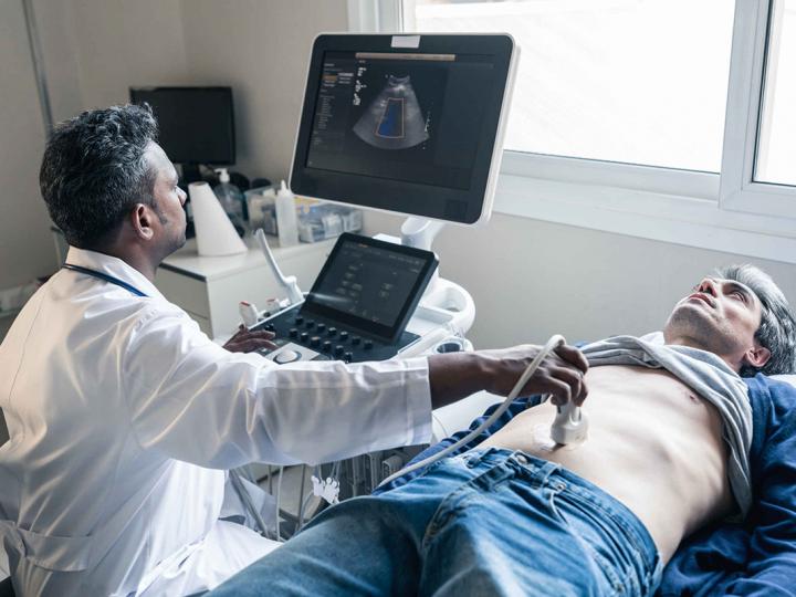 Ein Mann im mittleren Alter liegt auf einer Liege und lässt seinen Darm vom Arzt mittels Ultraschall untersuchen.