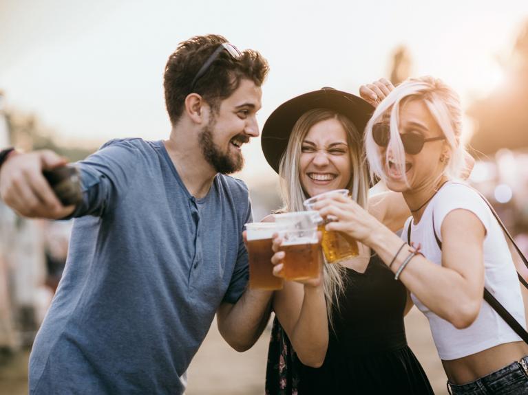 2 junge Frauen und ein junger Mann stoßen lächelnd mit Alkohol an