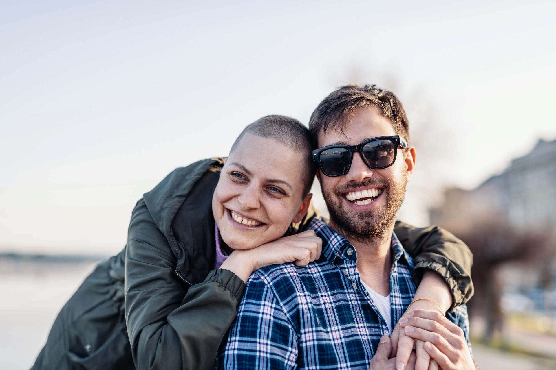 Krebskranke Frau steht in der Natur mit ihrem Freund und lächeln beide.