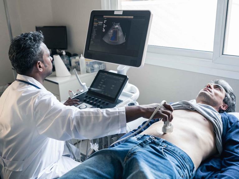Ein Mann im mittleren Alter liegt auf einer Liege und lässt seinen Darm vom Arzt mittels Ultraschall untersuchen.