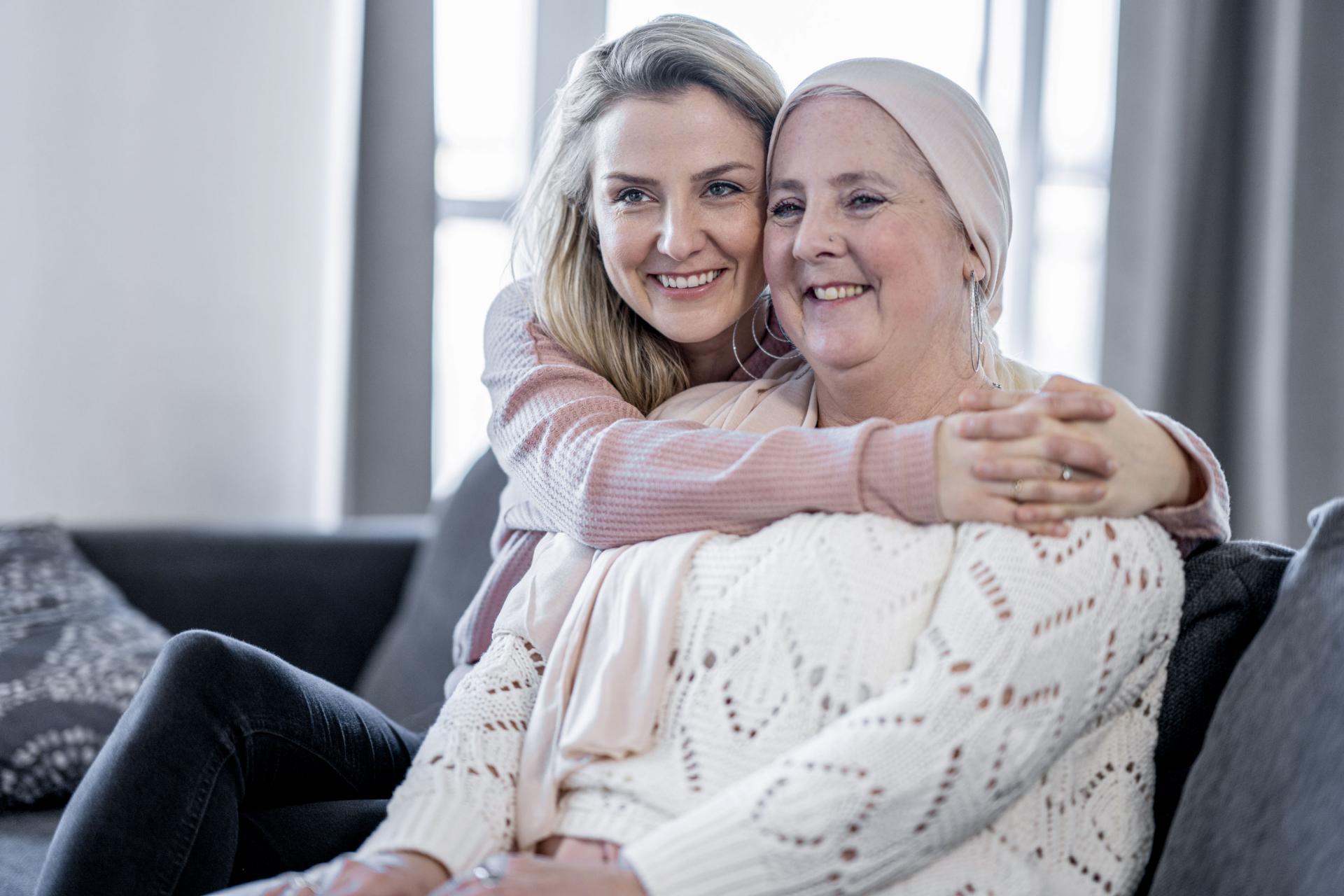 Krebskranke Mutter und Tochter sitzen auf der Couch und umarmen sich