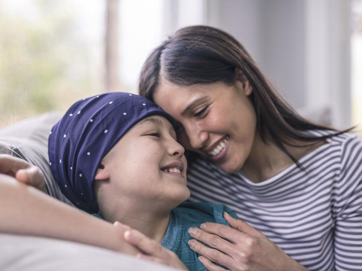 Eine Mutter und ihr Krebserkranktes Kind sitzen auf der Couch und sind glücklich.