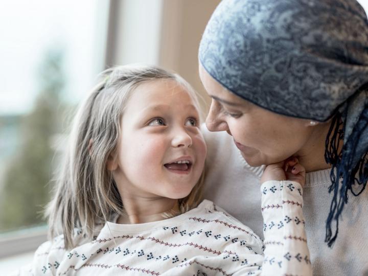 Frau, die an Krebs erkrankt ist, sitzt mit ihrer Tochter am Fenster und unterhält sich mit ihr