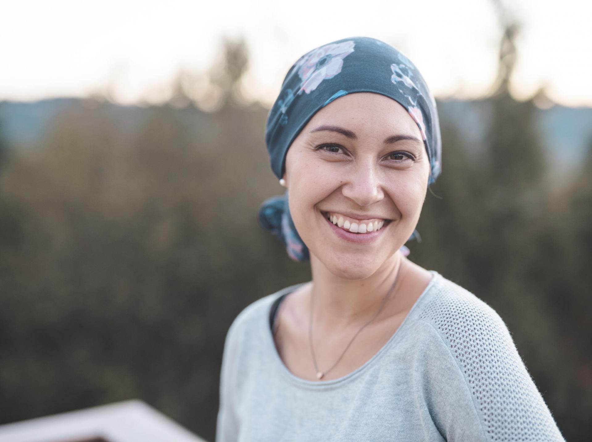 Eine junge Frau hat eine Krebserkrankung und trägt ein Kopftuch. Sie blickt in die Kamera und lächelt