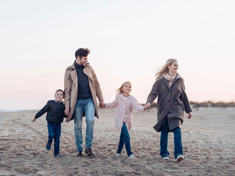 Eine vierköpfige lachende Familie spaziert am Strand entlang