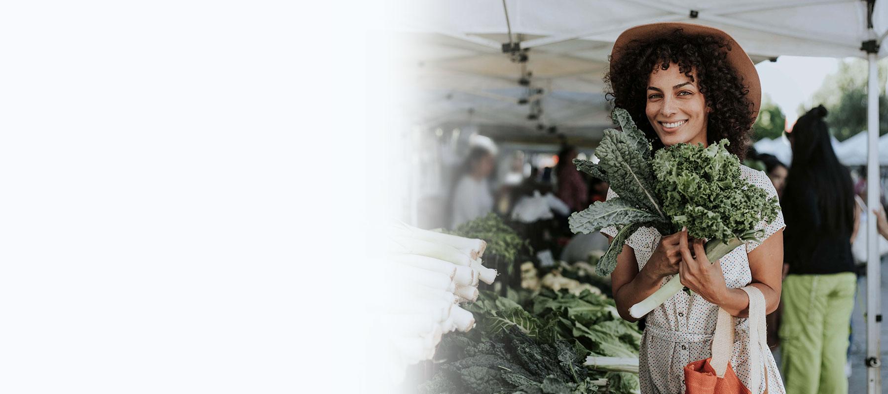 Eine Frau steht auf dem Wochenmarkt und hält grünes Gemüse in den Händen