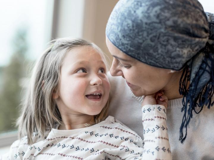 Frau, die an Krebs erkrankt ist, sitzt mit ihrer Tochter am Fenster und unterhält sich mit ihr