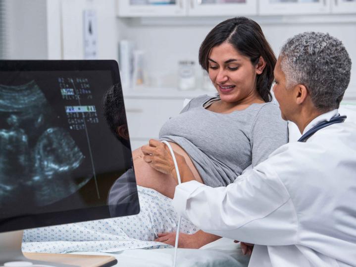 Eine schwangere Frau liegt auf der Untersuchungsliege bei der Gynäkologin und lässt einen Ultraschall machen.