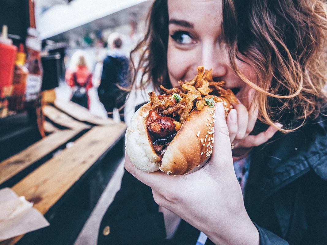 Eine Frau isst einen Hot Dog an einem Imbiss.