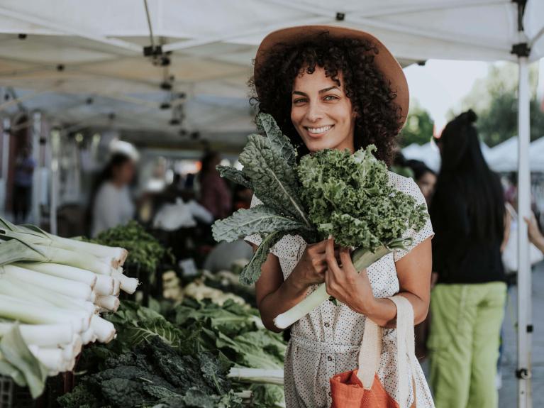 Eine Frau steht auf dem Wochenmarkt und hält grünes Gemüse in den Händen