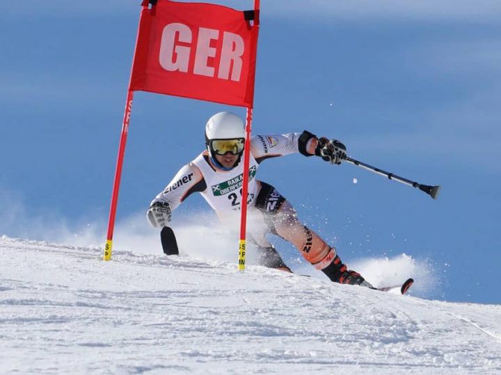 Amputierter Skifahrer hebt triumphierend seine Skier in die Höhe und lacht.